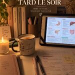 Une étudiante travaillant tard le soir sur son bureau avec des livres et un ordinateur.